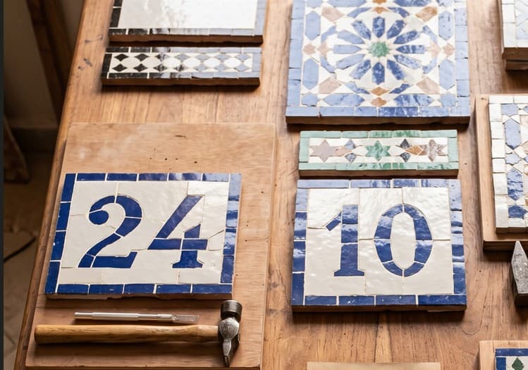 Two custom zellij house-number panels showing 24 and 10 in Fassi blue on white, laid on a workshop bench.