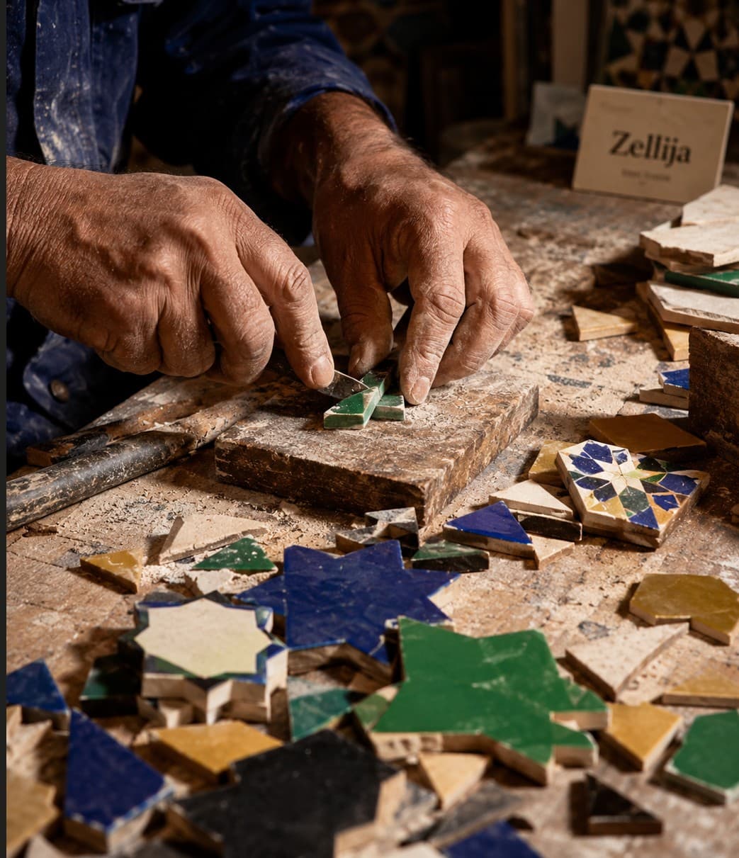 Close-up of a craftsman's hands placing a green star piece onto a zellij panel in the Fes workshop.